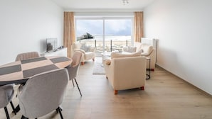 Een moderne hotelkamer met een groot raam, een zithoek en een eethoek, met uitzicht op zee.