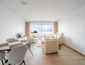 A modern hotel room with a large window, a dining area, and a seating area with a view of the sea. - Blankenberge Apartment for 4 (Blankenberge)
