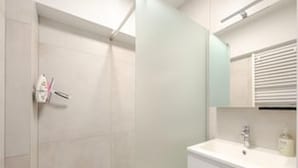 Een badkamer met een douche, wastafel en spiegel.