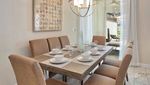 A dining area with a long table set for six, surrounded by six chairs, a chandelier, and a large abstract painting on the wall. - Sl4926 - 4BR House With Pool Near Disney Area (Kissimmee)