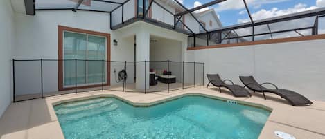 Una piscina con cerramiento de vidrio, sillas de descanso y una zona de estar cubierta con vistas al cielo.