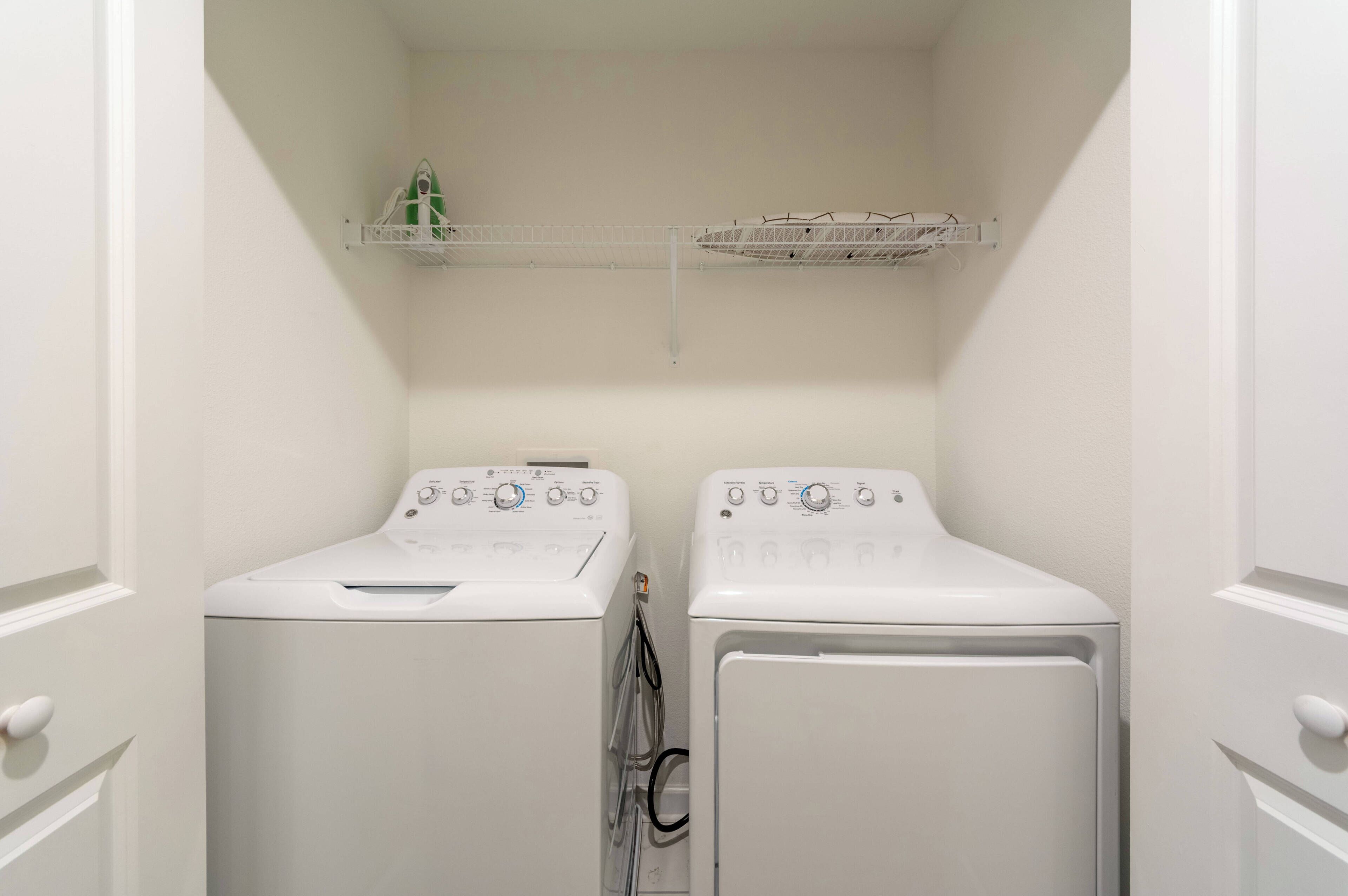 A laundry room with two white front-loading washing machines and two shelves above them.