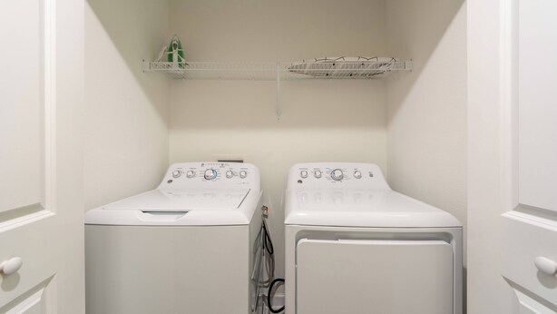 A laundry room with two white front-loading washing machines and two shelves above them. - Sl4926 - 4BR House With Pool Near Disney Area (Kissimmee)