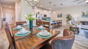 A dining area with a wooden table set for four, surrounded by chairs. There is a kitchen in the background with white cabinets and a microwave. - Sl3059 - 4BR House With Pool Near Disney (Kissimmee)
