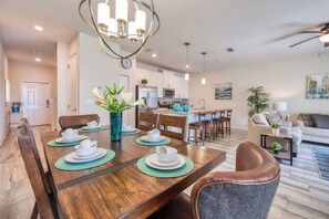 A dining area with a wooden table set for four, surrounded by chairs. There is a kitchen in the background with white cabinets and a microwave. - Sl3059 - 4BR House With Pool Near Disney (Kissimmee)