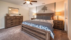 A bedroom with a bed, wooden dresser, nightstands, a ceiling fan, and a wall-mounted mirror. - Sl3059 - 4BR House With Pool Near Disney (Kissimmee)