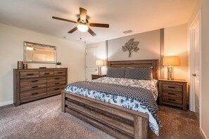 A bedroom with a bed, wooden dresser, nightstands, a ceiling fan, and a wall-mounted mirror. - Sl3059 - 4BR House With Pool Near Disney (Kissimmee)