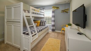 Una cama individual en literas con un escritorio y un televisor.