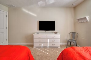 A bedroom with a white dresser, a television on top, a chair, and two beds with red bedding. - Sl3111 - 4BR House With Pool Near Disney Parks (Kissimmee)