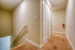 Ein Korridor mit beige gestrichenen Wänden, einem Teppichboden, einer weißen Tür und einem an der Wand befestigten Feuerlöscher.