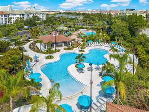 A resort with a large pool area, multiple lounge chairs, and a view of the surrounding cityscape. - Vcr2-409 Epic 3BR Condo Near Disney and Universal (Orlando)