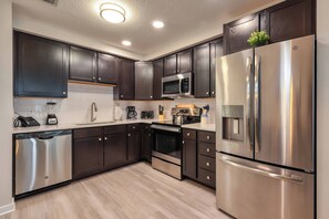 A modern kitchen with dark wooden cabinets, stainless steel appliances, and a light-colored countertop. - Vcr2-409 Epic 3BR Condo Near Disney and Universal (Orlando)