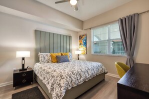 Quarto com uma cama, mesas de cabeceira, escrivaninha e janela com cortinas.