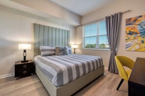 Une chambre à coucher moderne avec un lit, des tables de chevet, une fenêtre avec des rideaux et un tableau au mur.