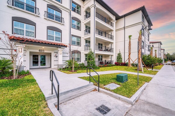 A multi-story residential building with balconies, a well-maintained lawn, and a clear sky. - Vcr1-408 - 3BR Condo Near Disney and Universal (Orlando)