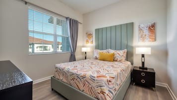A modern bedroom with a bed, two bedside tables, a nightstand, a window with curtains, and artwork on the walls.