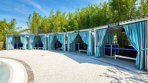 Mehrere überdachte Außenbereiche mit blauen Vorhängen, ein Schwimmbecken und eine Terrasse aus Ziegelsteinen.