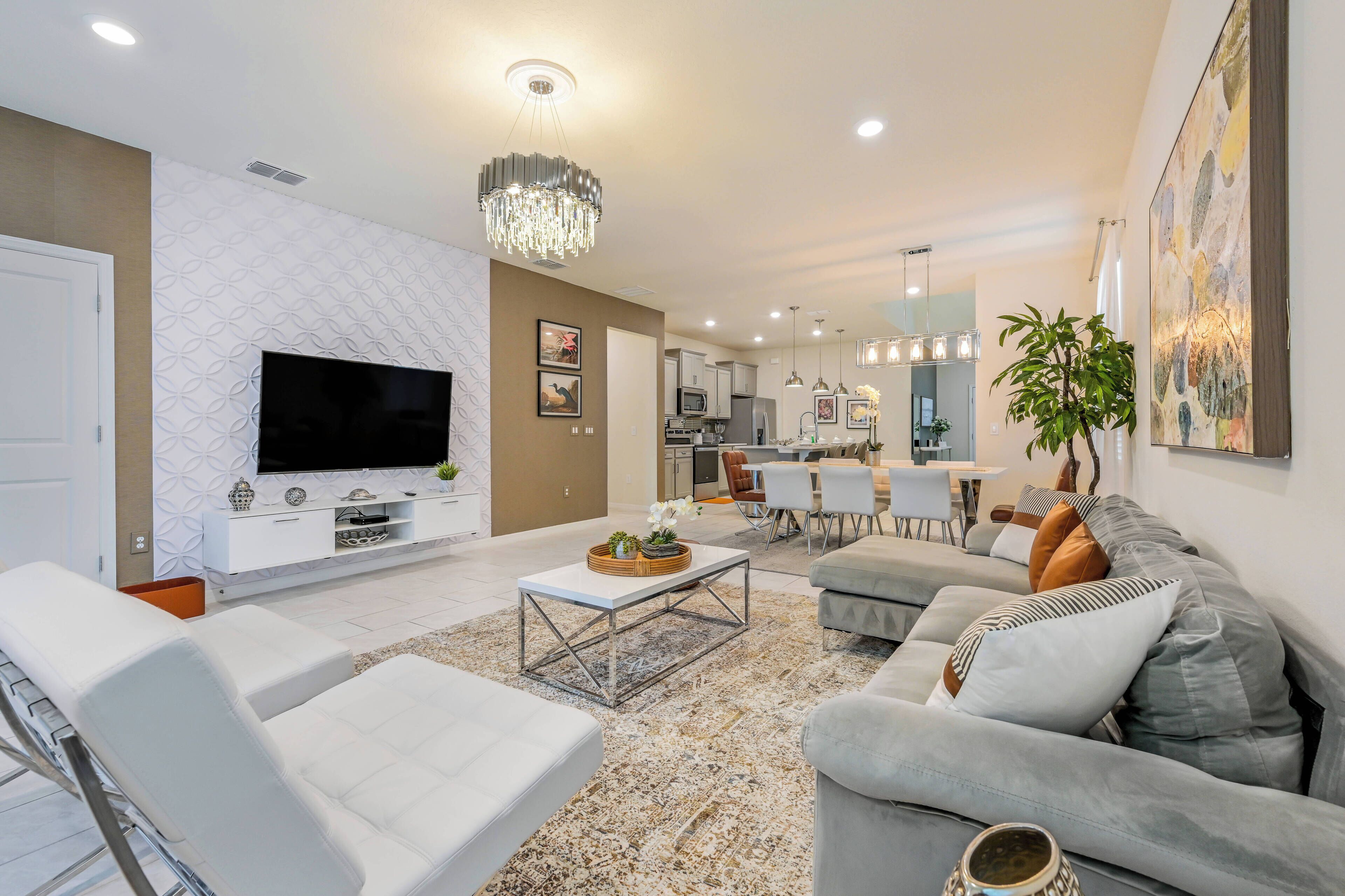 A modern living room with a flat-screen TV, white sofas, a coffee table, and a dining area with chairs and a table.