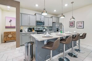 A modern kitchen with grey cabinets, stainless steel appliances, and a central island with bar stools. - Wi1196 - 7BR House With Pool Near Disney (Davenport)
