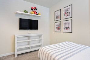 A bedroom with a bed, a TV mounted on a wall, a white shelf with a plush toy, and framed pictures on the wall. - Wi1196 - 7BR House With Pool Near Disney (Davenport)