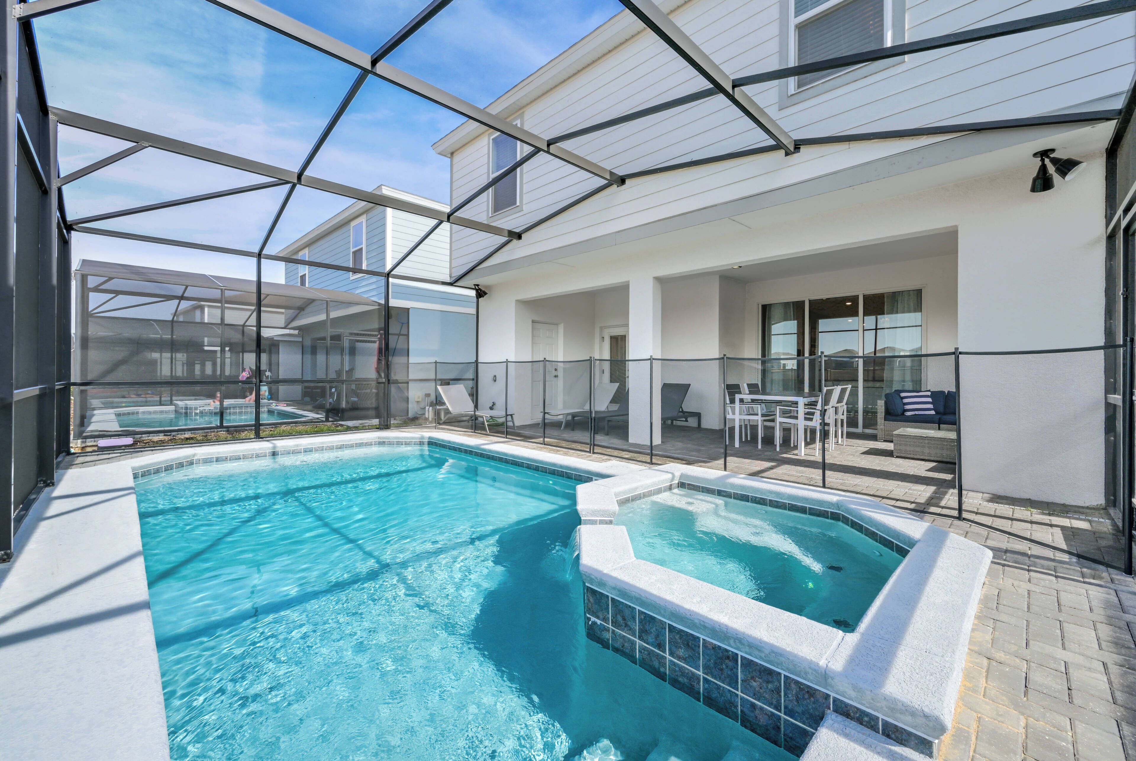 A swimming pool with a glass enclosure, a hot tub, and outdoor seating.