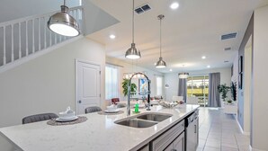 A modern kitchen with a large island, stainless steel appliances, pendant lighting, and a view to the living area. - Wi1196 - 7BR House With Pool Near Disney (Davenport)
