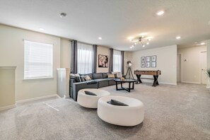 A living room with a sectional sofa, two white ottomans, a coffee table, and a pool table. - Wi1196 - 7BR House With Pool Near Disney (Davenport)