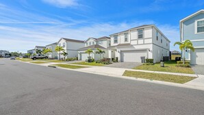 A residential street with modern houses, a clear sky, and a well-maintained lawn. - Wi1196 - 7BR House With Pool Near Disney (Davenport)