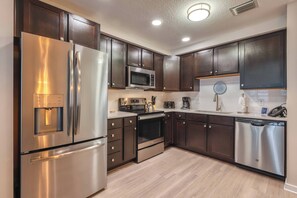 A modern kitchen with stainless steel appliances, dark wooden cabinets, and a light-colored countertop. - Vcr2-310 - 3BR Condo Near Disney and Universal (Orlando)