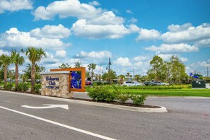 Schild des Hideaway Club am Story Lake, mit einer Straße dorthin, umgeben von Palmen und blauem Himmel.