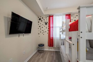 Ein Zimmer mit Etagenbetten, einem Fernseher, einem kleinen runden Tisch und einem Fenster mit roten Vorhängen.