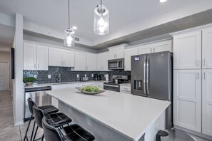 Een moderne keuken met witte kasten, roestvrijstalen apparatuur en een centraal kookeiland met barkrukken.