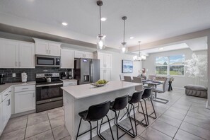 A modern kitchen with white cabinets, stainless steel appliances, and a central island with bar stools. - Sl3111-106 - 2BR Apartment Near Disney Attractions (Kissimmee)