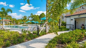 A pool area with lounge chairs and umbrellas, surrounded by palm trees and greenery. - Vcr2-204 - 3BR Condo Near Disney and Universal (Orlando)