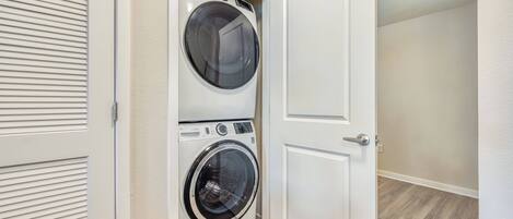 A laundry room with a front-loading washer and dryer, a door, and a wooden floor.