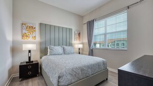 A modern bedroom with a bed, two bedside tables with lamps, and a window with curtains. - Vcr4-410- 3BR Condo With Resort Access Near Disney (Orlando)