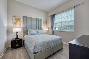 A modern bedroom with a bed, two bedside tables with lamps, and a window with curtains. - Vcr4-410- 3BR Condo With Resort Access Near Disney (Orlando)