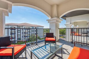 A balcony with wicker furniture and a glass table, overlooking a residential area with a building in the background. - Vcr4-410- 3BR Condo With Resort Access Near Disney (Orlando)