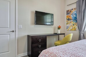 Ein Hotelzimmer mit Bett, Schreibtisch, Flachbildfernseher, Stuhl, Kommode und einem Bild an der Wand.