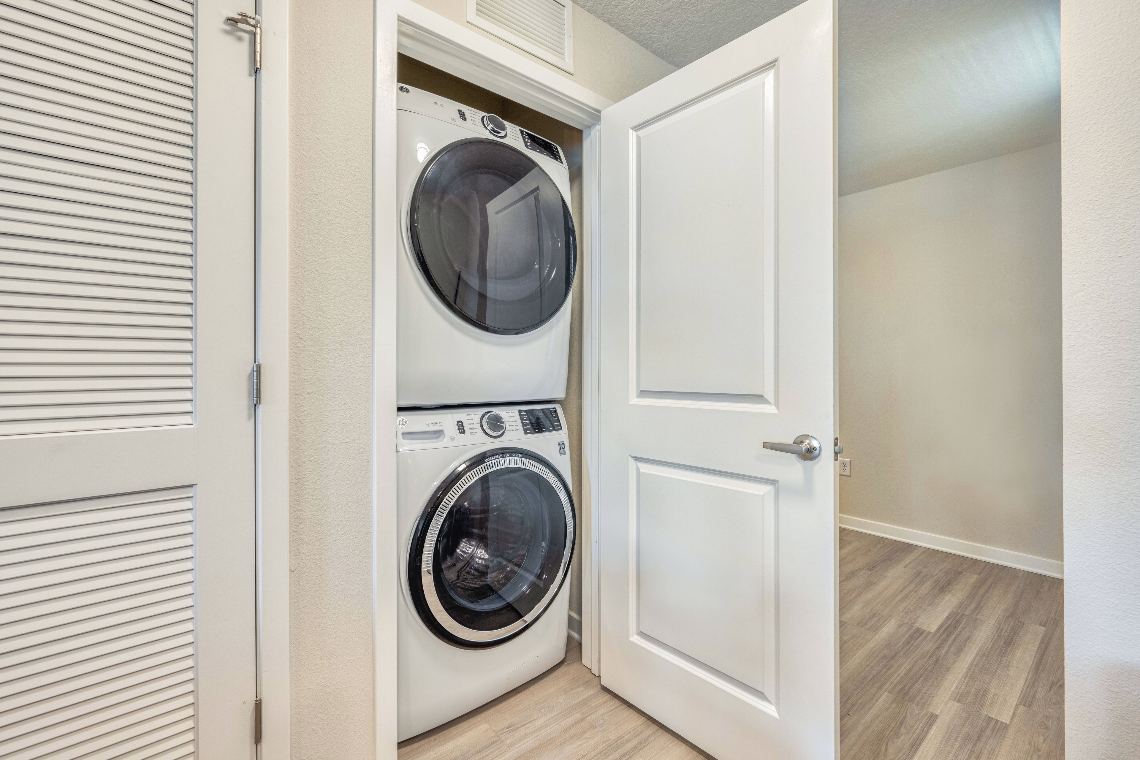 A laundry room with a front-loading washer and dryer, a door, and a wooden floor.