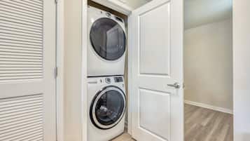 A laundry room with a front-loading washer and dryer, a door, and a wooden floor.