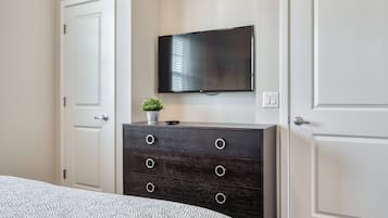 Een slaapkamer met een bed, een donkere houten dressoir, een flatscreen televisie aan de muur en een kleine plant in een potje op het dressoir.