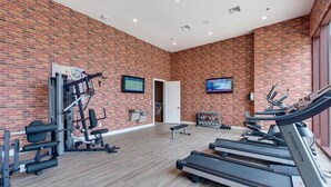 A gym with brick walls, treadmills, weight machines, and a door leading to another room. - Mvy7664 - 3BR House Near Disney With Hot Tub (Kissimmee)