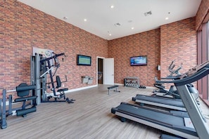 Un gimnasio con paredes de ladrillo, cintas de correr, máquinas de pesas y una puerta que conduce a otra sala.