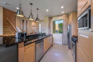 Uma cozinha moderna com ilha central, eletrodomésticos de aço inoxidável, iluminação pendente e vista para o exterior.