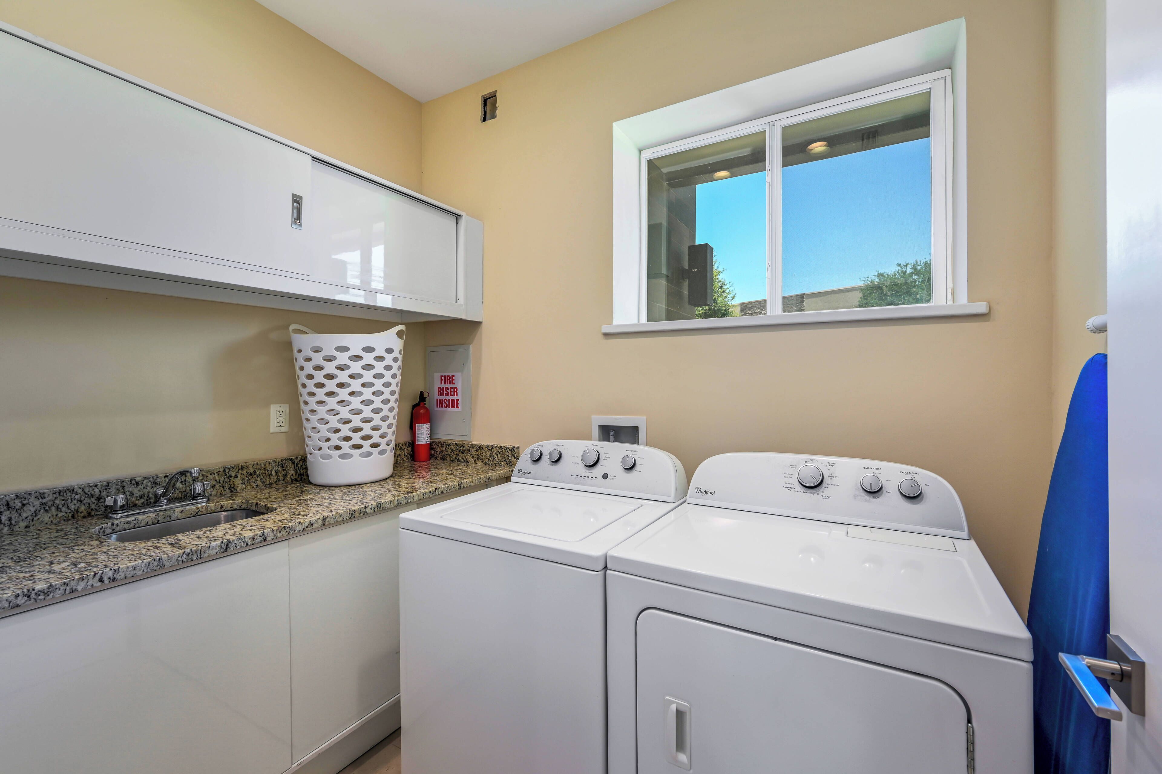 A laundry room with a sink, a white washing machine, a dryer, and a window with a view of the sky.