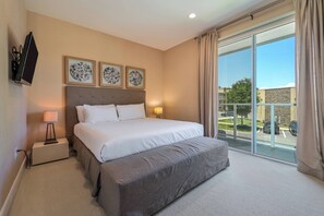 A hotel room with a large bed, a bedside table with a lamp, a flat-screen TV mounted on the wall, and a view of the outside through a large window. - Mvy7664 - 3BR House Near Disney With Hot Tub (Kissimmee)