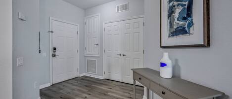 A hallway with a wooden floor, white doors, a light switch, and a framed abstract painting on the wall.