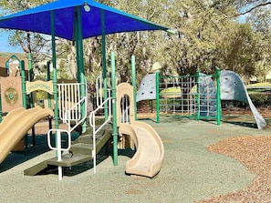 A playground with a blue canopy, a slide, and climbing structures. - Ld12108 - 4BR Apartment Near Disney (Kissimmee)