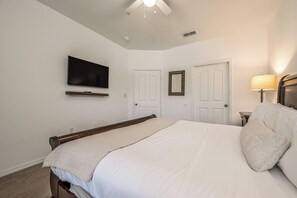 Un dormitorio con cama, televisor montado en la pared, dos puertas y una lámpara.